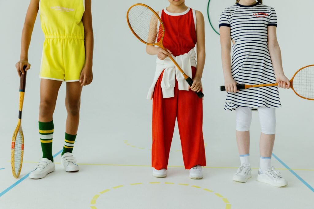 Three children holding rackets, showcasing colorful sportswear on an indoor court.
